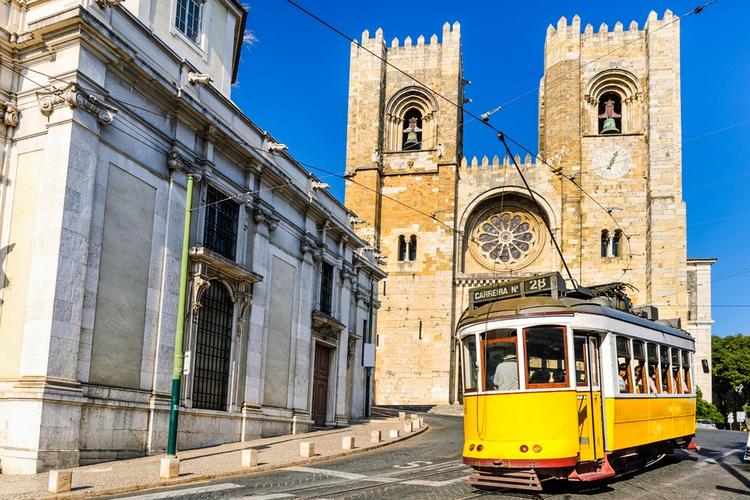 Zabytkowy żółty tramwaj przed katedrą w Lizbonie, Portugalia